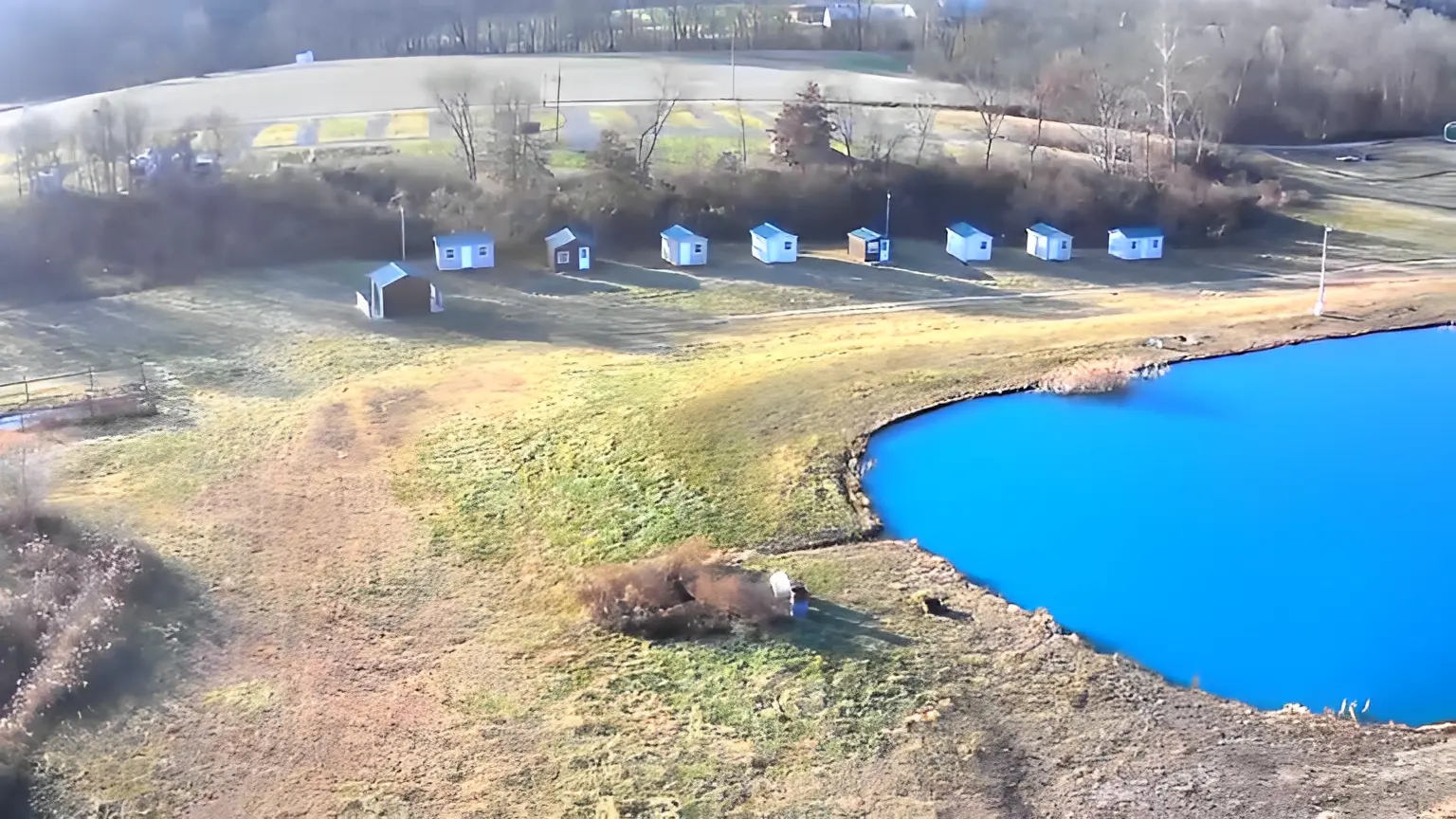 Rural landscape with cabins and blue pond.